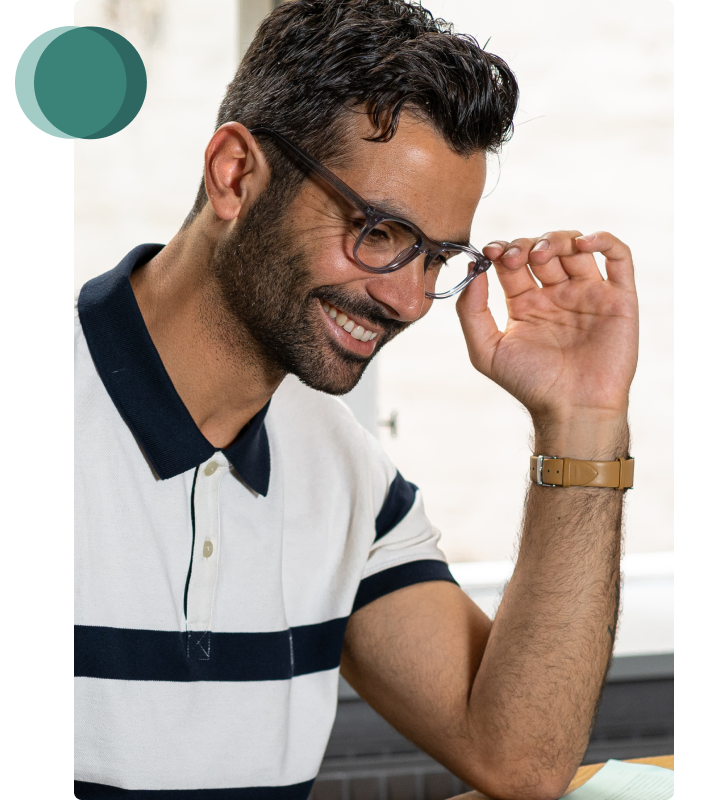 Stilig man i randig skjorta sitter vid bord och läser en tidning med Luxreaders läsglasögon och ett leende på läpparna